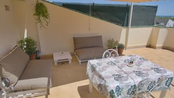 An outdoor patio with a sofa, a small table, and a dining table with chairs.