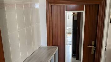 Un couloir avec un sol carrelé de carreaux blancs, une porte en bois et un meuble blanc avec des étagères.