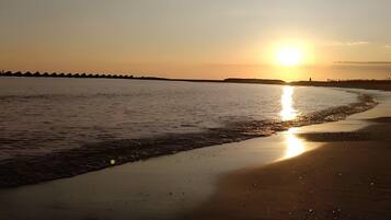 A beach with a sunset, calm water, and a distant shoreline.