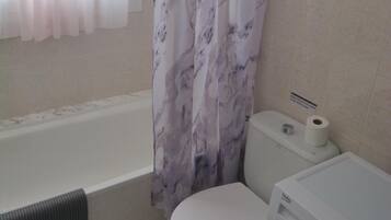 A bathroom with a bathtub, toilet, and washing machine.