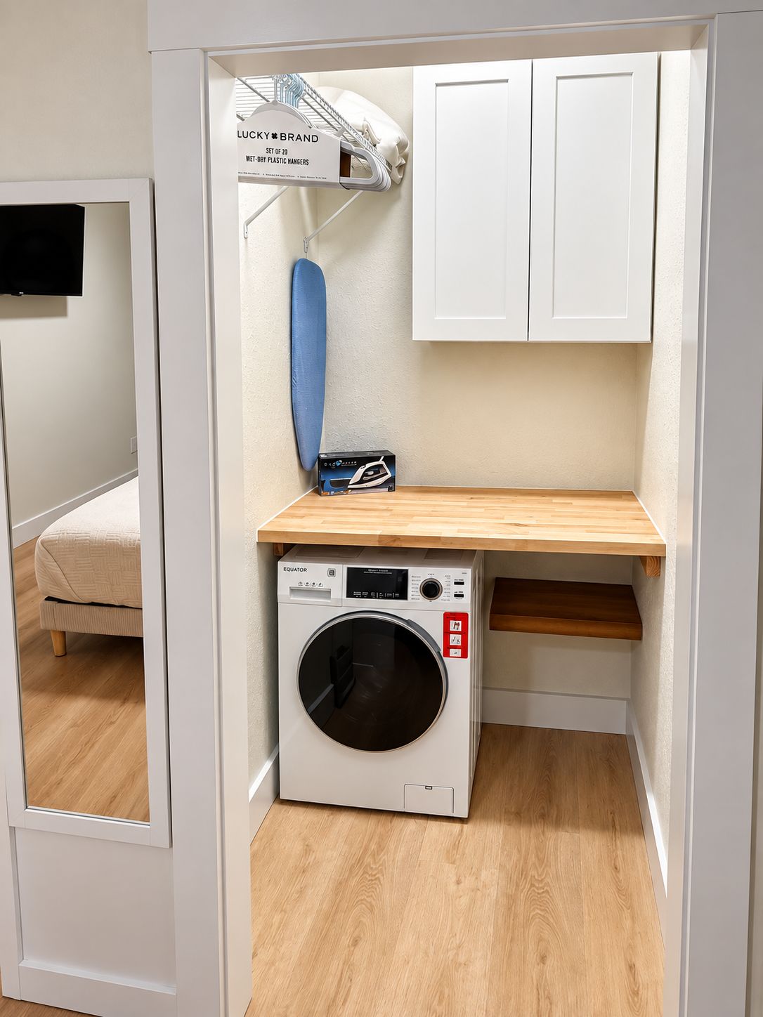 Une petite buanderie comprenant un lave-linge, un étendoir et une petite étagère en bois.