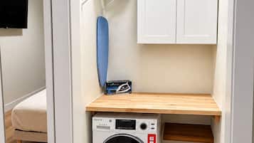 Une petite buanderie comprenant un lave-linge, un étendoir et une petite étagère en bois.