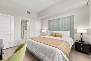 A modern bedroom with a large bed, bedside lamps, a nightstand, and a green chair. - Orlando for Work or Play, Comfortable 3BR condo (Orlando)