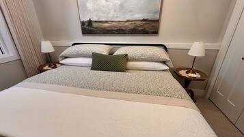 A neatly made bed with a pillow, a bedside lamp, and a painting on the wall.