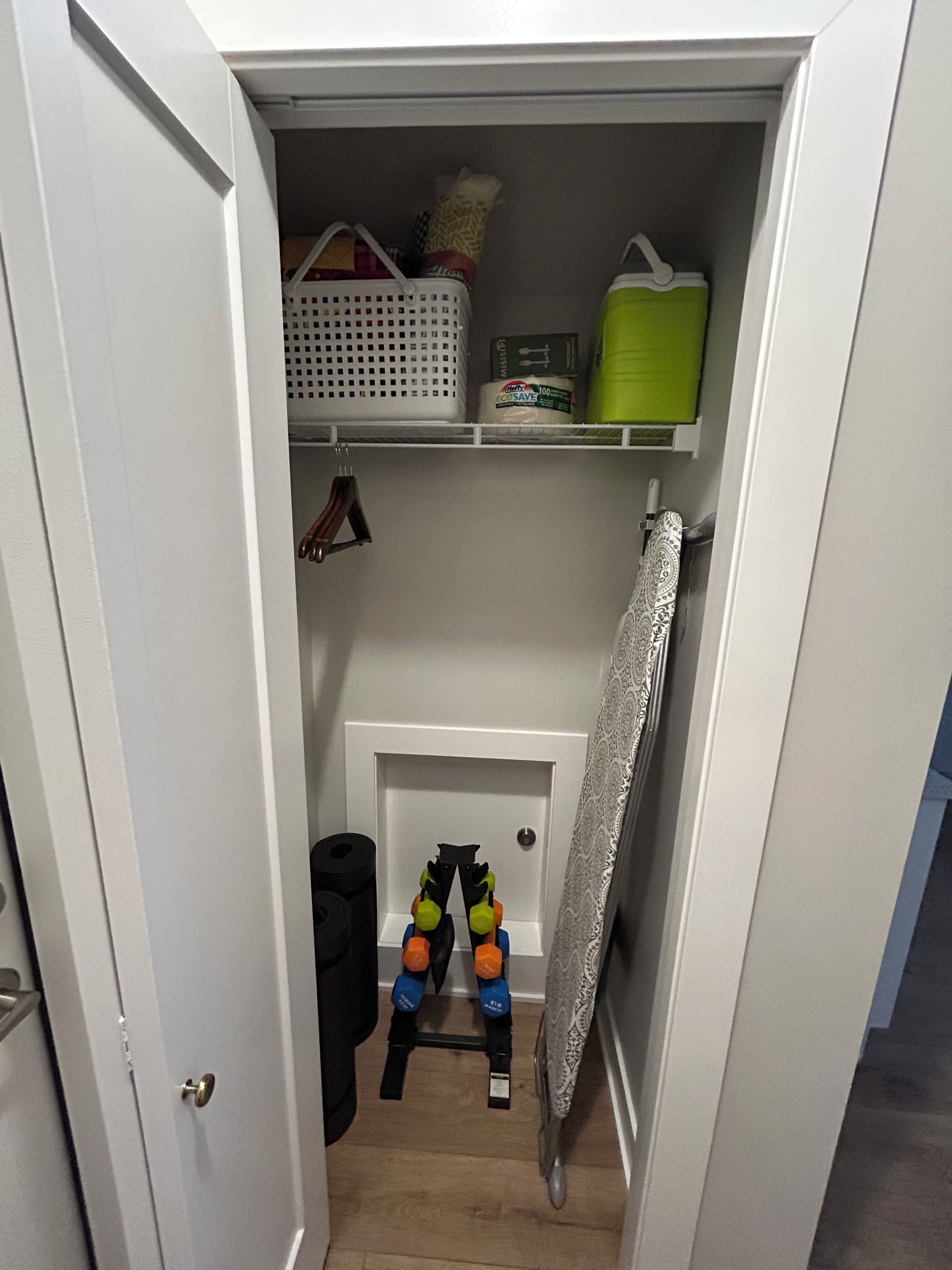 A narrow hallway with a door leading to a closet containing shelves with storage baskets, a green container, and a roll of toilet paper.