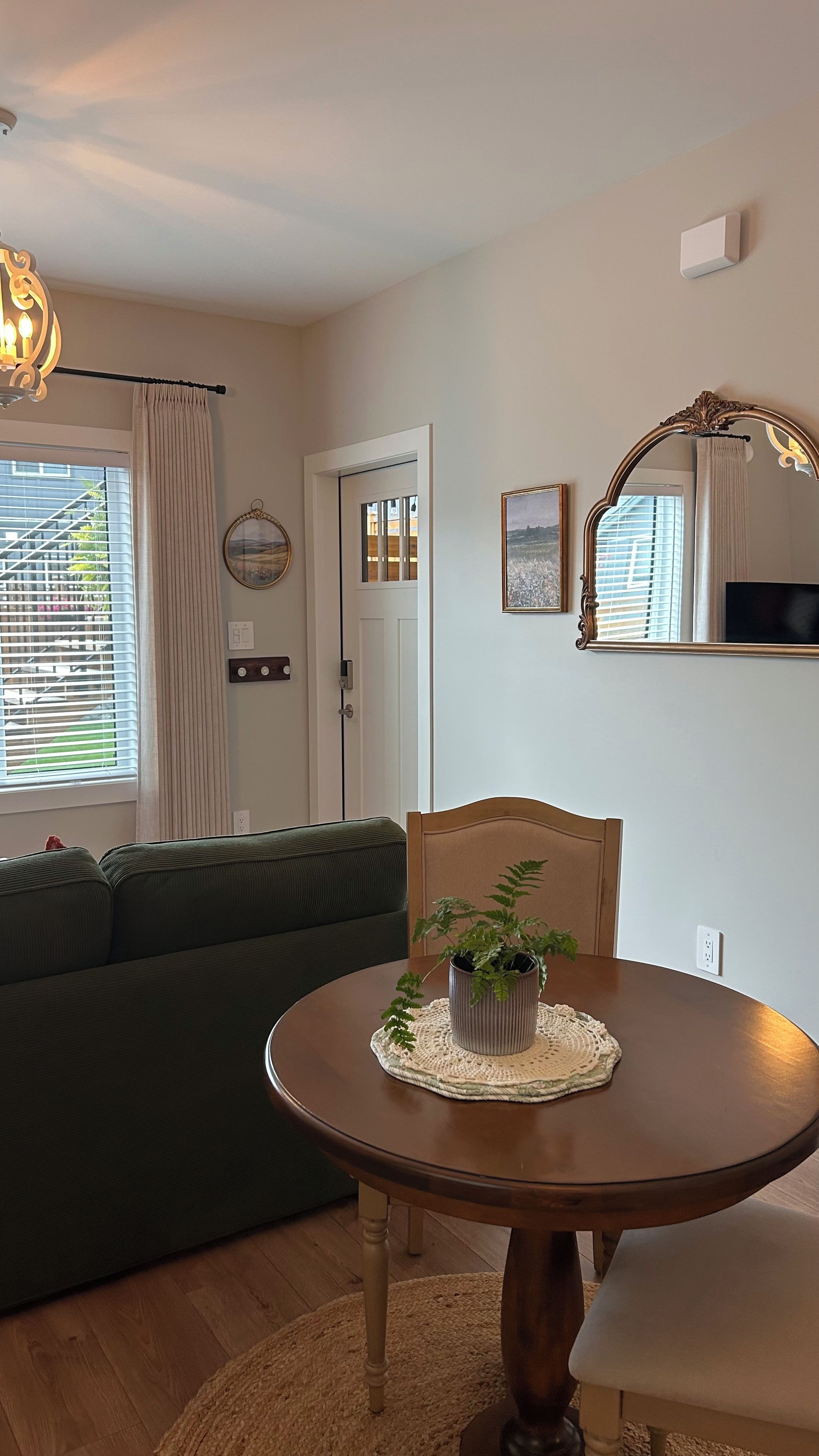 A living room with a green sofa, a round wooden table with a plant, and a mirror on the wall.