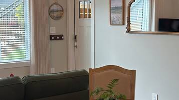A living room with a green sofa, a round wooden table with a plant, and a mirror on the wall.