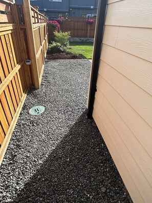 A gravel pathway leading to a wooden gate, with a manhole cover visible. - Fall Escape for 2 • King Bed • Fireplace • 
Heated Private Patio • Free Parking (Victoria)