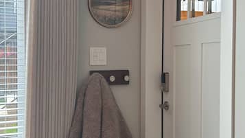 Ein Zimmer mit einer weißen Tür, einem Fenster mit Jalousien, einem an der Wand hängenden Bilderrahmen, einem Handtuch an einem Haken und einem gemusterten Teppich auf dem Boden.