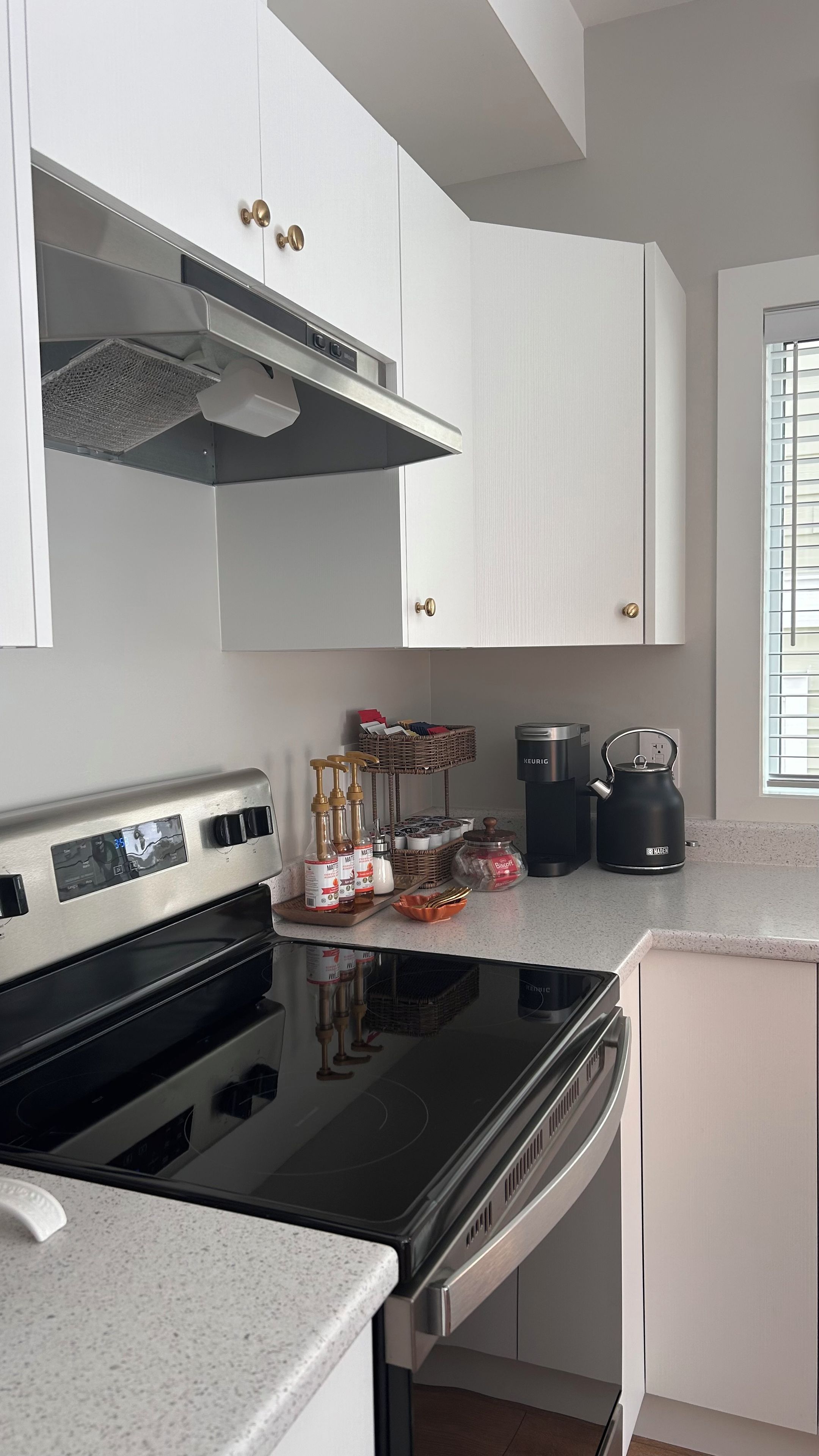 A modern kitchen with stainless steel appliances, white cabinetry, and a window with blinds.