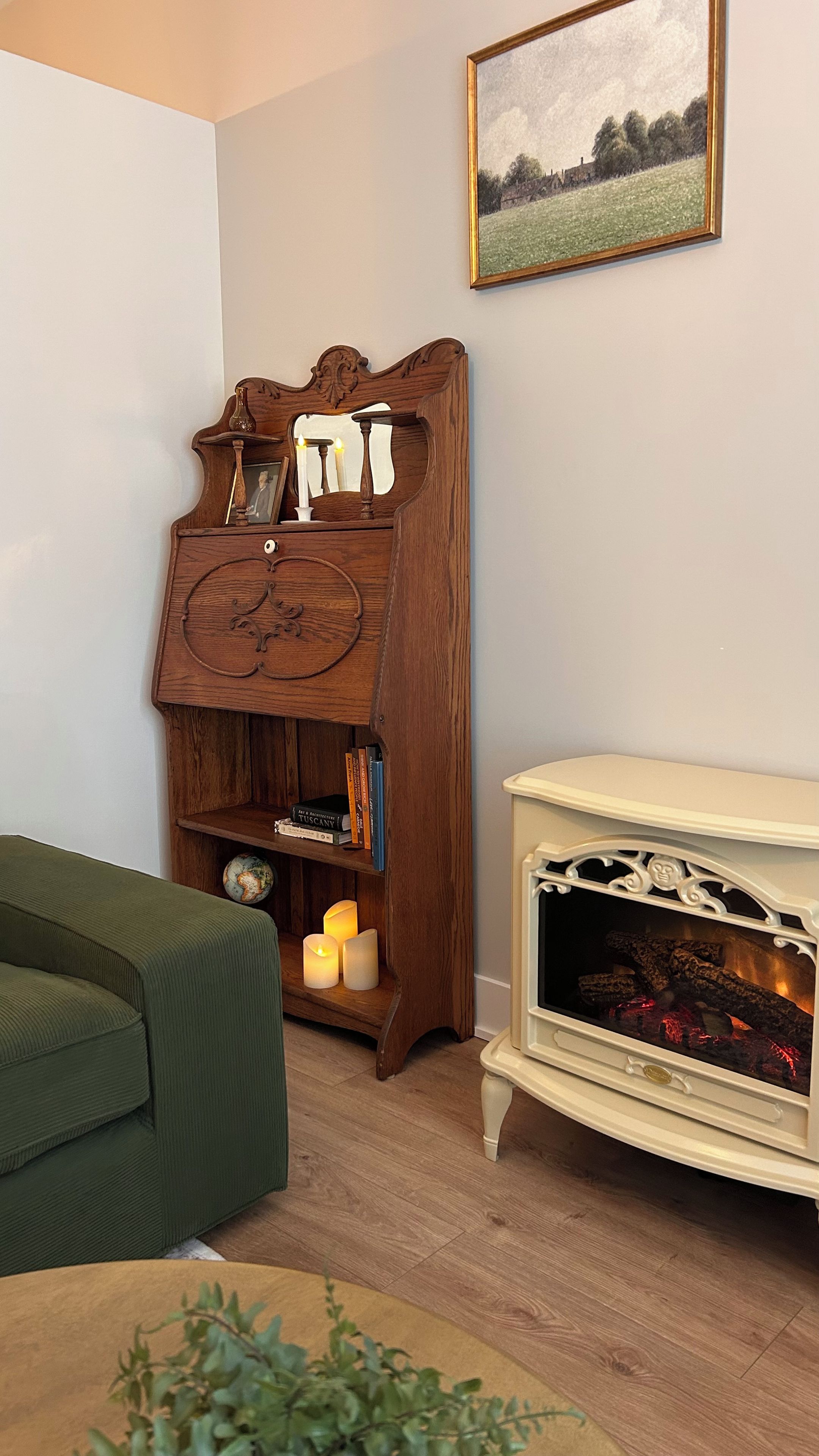 Een kamer met een houten boekenkast, een groene bank, een witte haard en een lijst met een landschap op de muur.