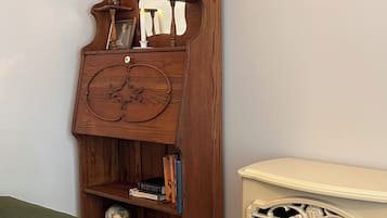 Een kamer met een houten boekenkast, een groene bank, een witte haard en een lijst met een landschap op de muur.