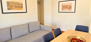 A living room with a grey sofa, a wooden dining table with chairs, and two framed pictures on the wall. - Cute apartment in Acropolis (Athens)