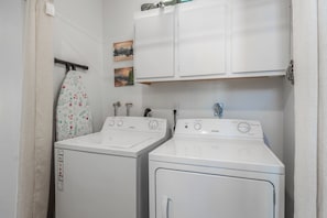 A laundry room with two front-loading washing machines and a dryer. There is a hanging rack with a floral-patterned cloth. - Close to Downtown | Fireplace (Mammoth Lakes)