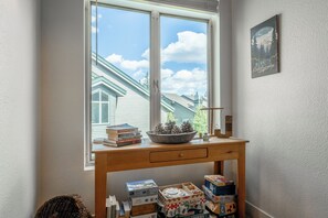 A room with a wooden desk, a window with a view of houses, and a framed picture on the wall. - Close to Downtown | Fireplace (Mammoth Lakes)