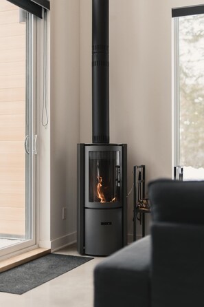 A modern living room with a black wood-burning stove, a glass door, and a view of the outdoors. - Outdoors | Light | Fire | King-Size Bed | Dog | Ski-In (Saint-Côme)