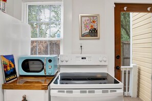 A compact kitchen with a microwave, oven, and a window with blinds. - Oakleighs Little Cottage (Mobile)