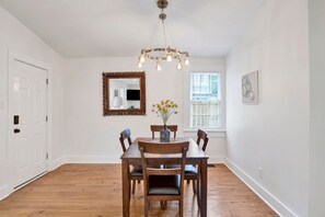 A dining area with a wooden table and chairs, a mirror, and a window with blinds. - Oakleighs Little Cottage (Mobile)