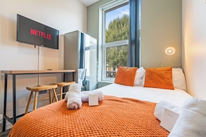 A hotel room with a bed, a desk, a TV, and a window. - Sutherland Apartments - Apt 15 (London)