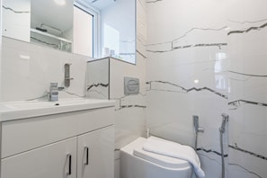 Ein modernes Badezimmer mit einem weißen Waschtisch, einem Spiegel, einer Toilette und einer Duschkabine.