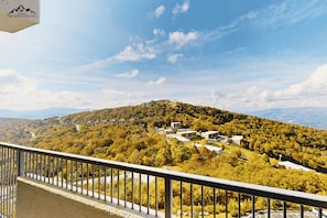 Paisaje montañoso con zona residencial que muestra varios edificios, cielo despejado y barandilla de balcón.