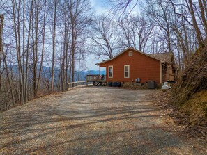 A red cabin with a porch and a gravel driveway leading to it, surrounded by trees and a mountainous backdrop. - Dreamweaver a serene cabin spectacular Mountain View's in charming Bryson City. (Bryson City)