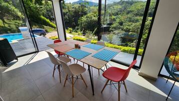 Een eethoek met een tafel en stoelen, grote ramen met uitzicht op groen en een zwembad.