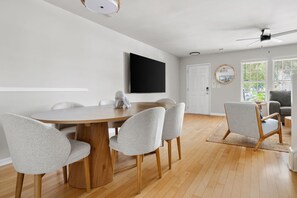 A modern dining area with a wooden table and grey upholstered chairs, a mounted flat-screen TV, and a ceiling fan. - Rhythm & Tide-concerts. Coastlines. Charleston (Charleston)