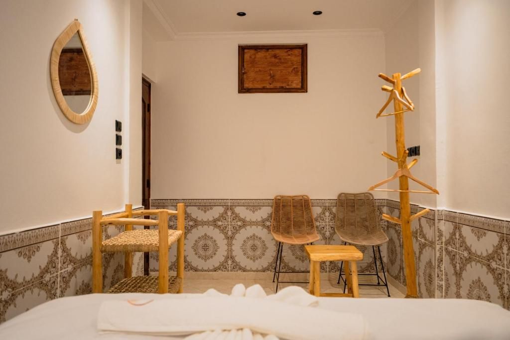 A hotel room with a bed, two chairs, a wooden coat rack, a mirror, and a wall-mounted picture.