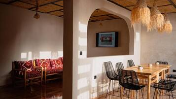 A dining area with a wooden table and chairs, a sofa with patterned cushions, and a ceiling with woven light fixtures.