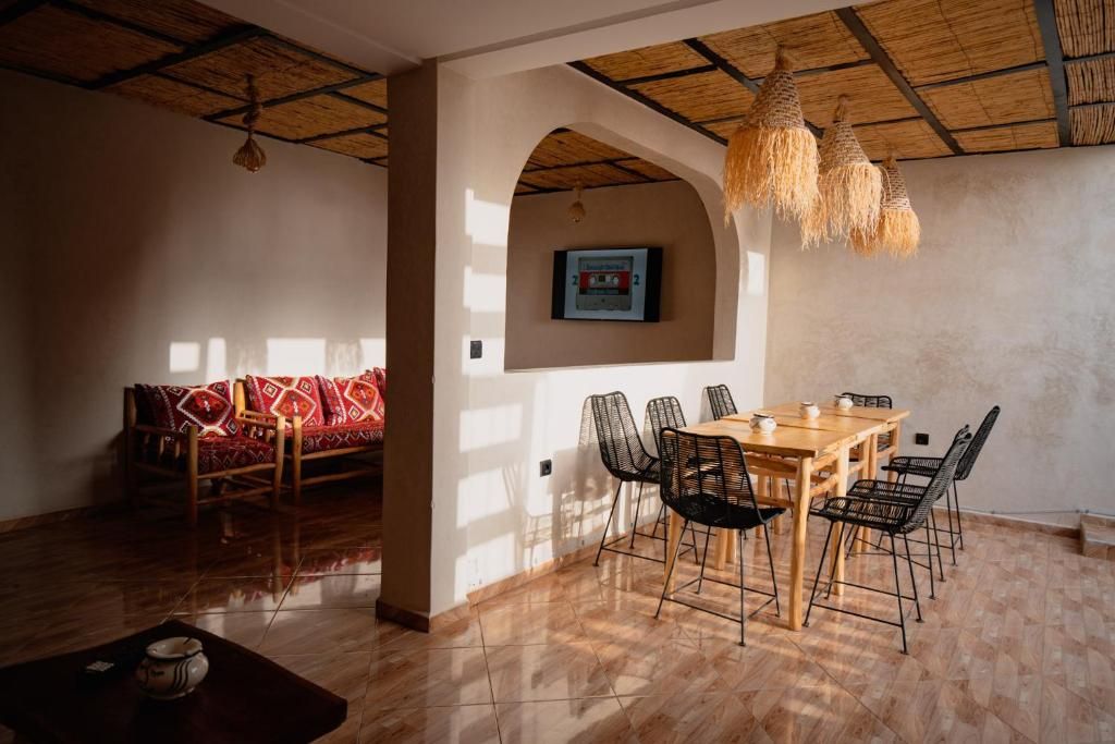 A dining area with a wooden table and chairs, a sofa with patterned cushions, and a hanging light fixture.