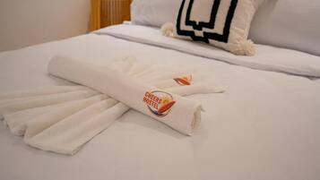 A neatly made bed with a white duvet and a towel with a logo.