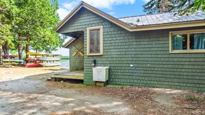 A small cabin with a sloped roof, a window, and a door. There is a dock with canoes in the background. - The Cabins on Webb Pond - NEW! Waterfront (Eastbrook)