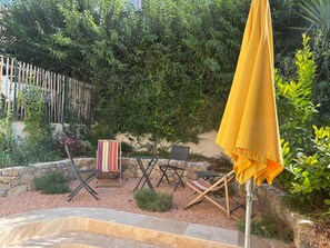 Un espace extérieur aménagé avec des sièges, un parasol jaune, des murs en pierre et une variété de plantes.