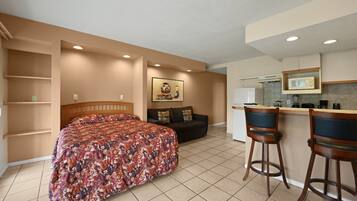 A hotel room with a bed, a sofa, a kitchenette, and a painting on the wall.