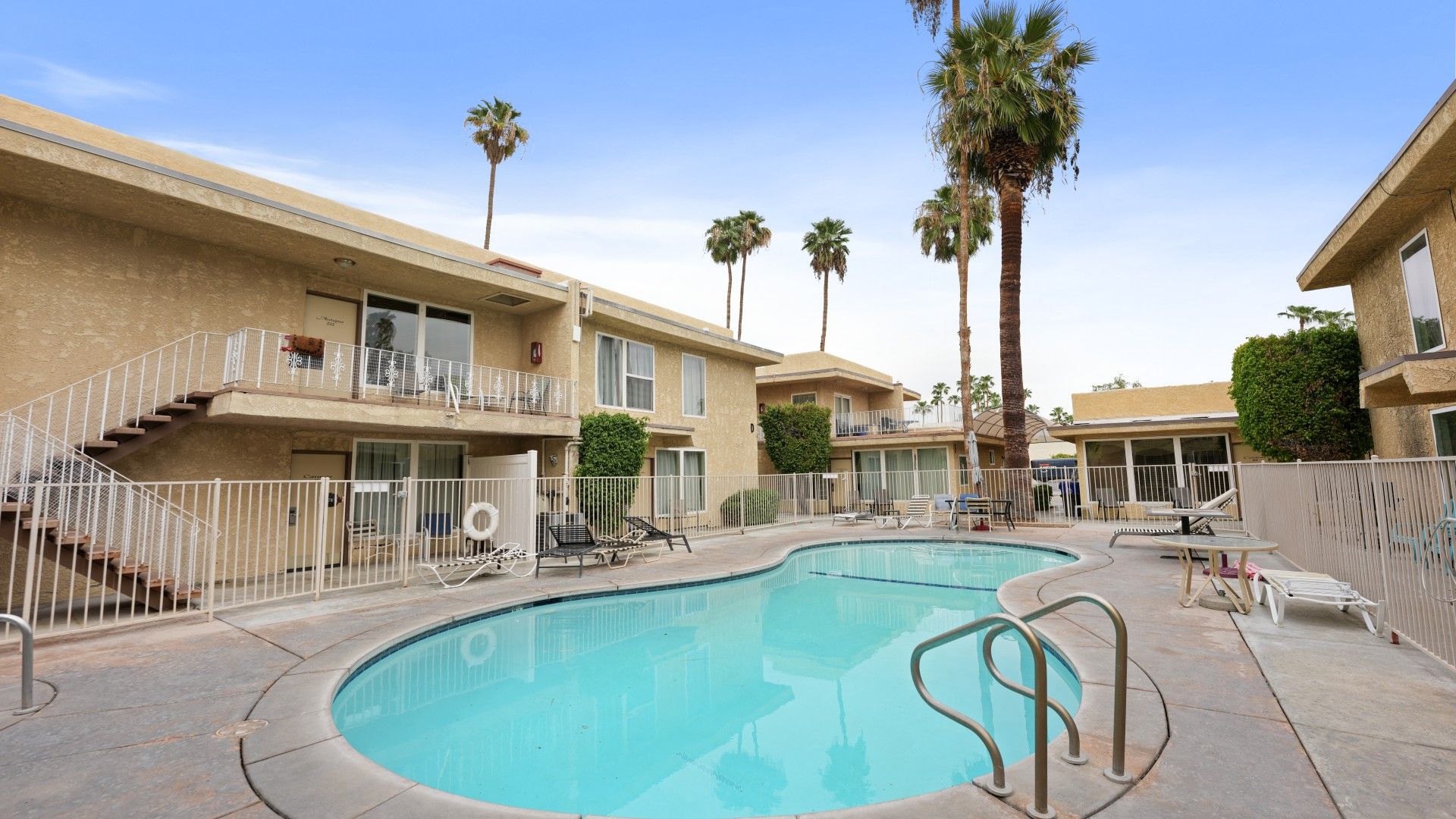 A pool area with a clear blue pool, a white fence, and a building with balconies.