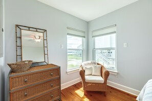 A room with a ceiling fan, a wicker dresser, a chair with cushions, and a large window with a view of a balcony. - 2nd Row Getaway with Gulf Views, Coastal Charm & Easy Beach Access (Galveston)