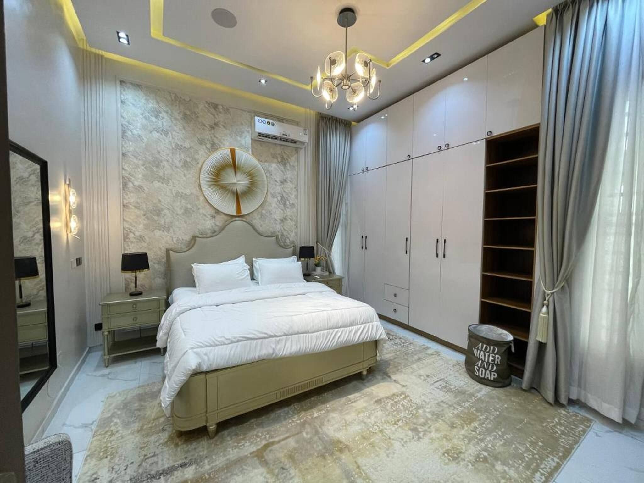A bedroom with a large bed, a wardrobe, a mirror, and a chandelier.