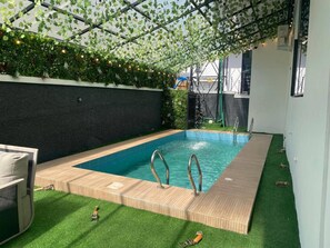 A swimming pool with a wooden deck, surrounded by artificial grass and a black wall. - Luxury 5 BR Villa With Cinema and Pool (Lekki)