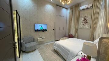 Una habitación de hotel con una cama, televisión, silla, escritorio y un elemento decorativo en la pared.