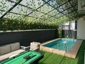 Un área de piscina interior con mesa de billar verde, sillas de descanso y un jardín en el techo.