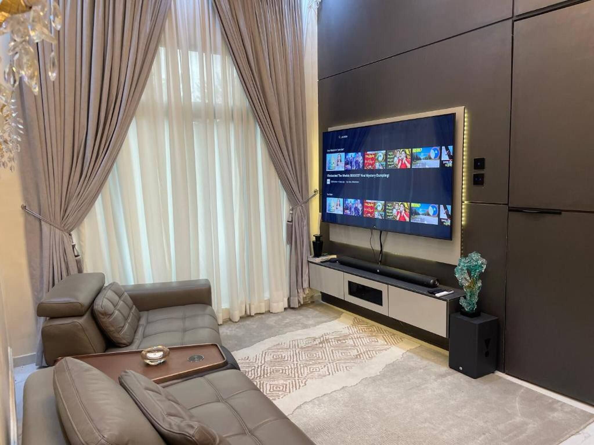 Una sala de estar moderna con un televisor de pantalla plana grande montado en la pared, un sofá modular, una mesa de centro y una escultura de vidrio decorativa.
