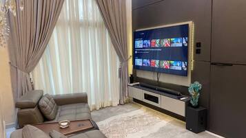 Una sala de estar moderna con un televisor de pantalla plana grande montado en la pared, un sofá modular, una mesa de centro y una escultura de vidrio decorativa.