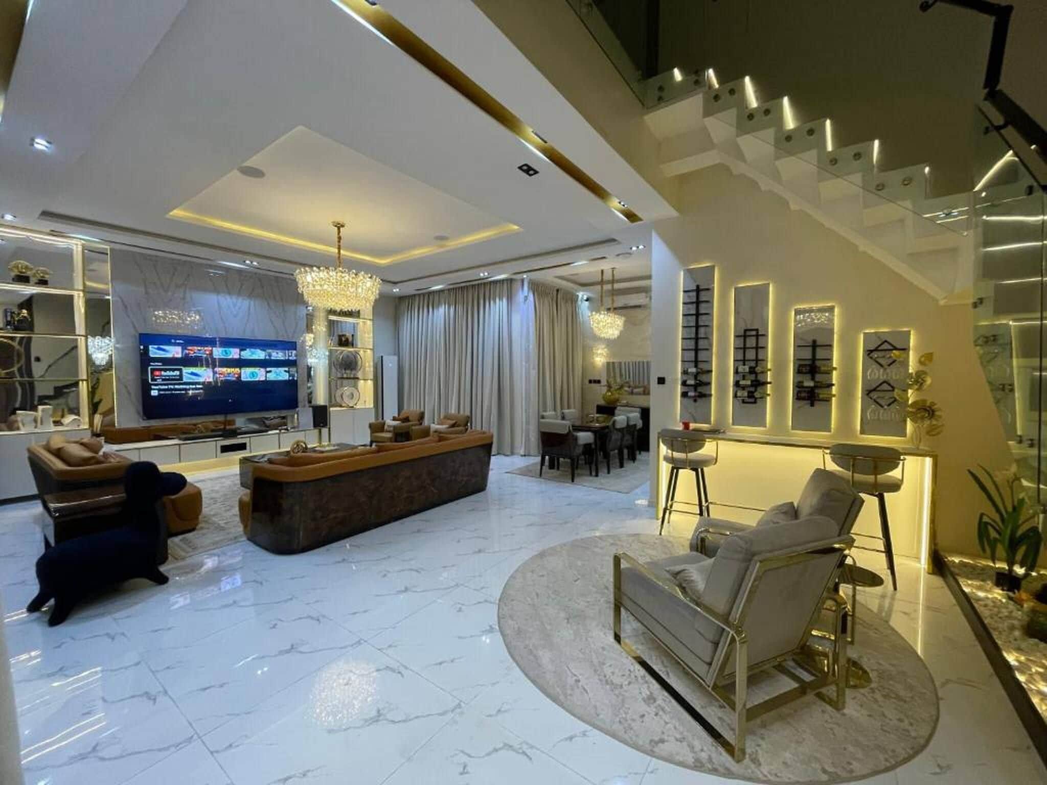 Una sala moderna con un televisor grande, un sofá, una mesa de centro y un comedor con sillas.