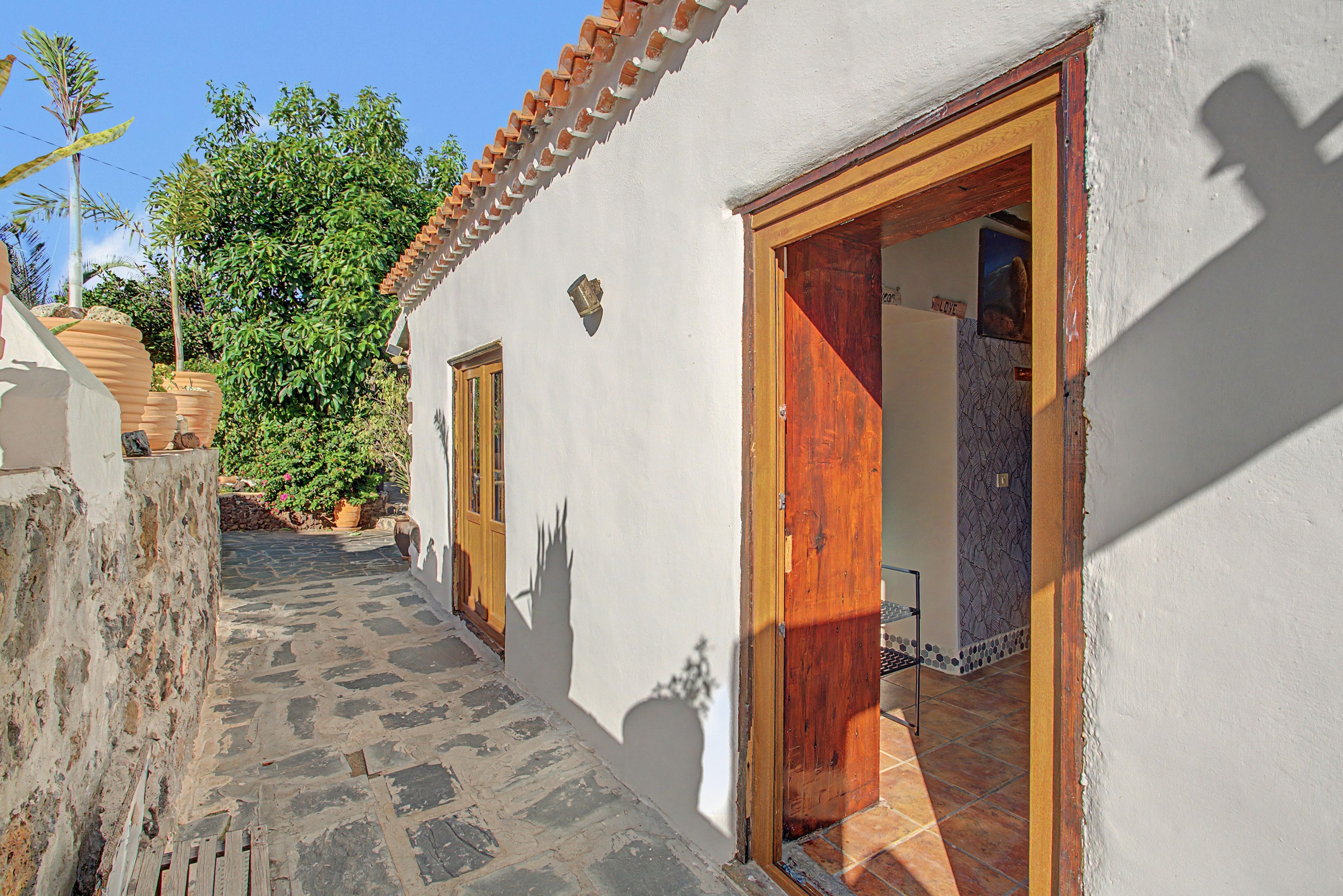 Un étroit sentier pavé de pierres mène à un bâtiment blanc doté d’un toit en tuiles et de portes en bois.