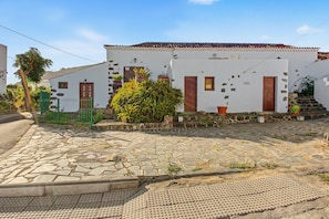 Un bâtiment blanc avec des portes et des fenêtres rouges, une cour pavée et une clôture verte.