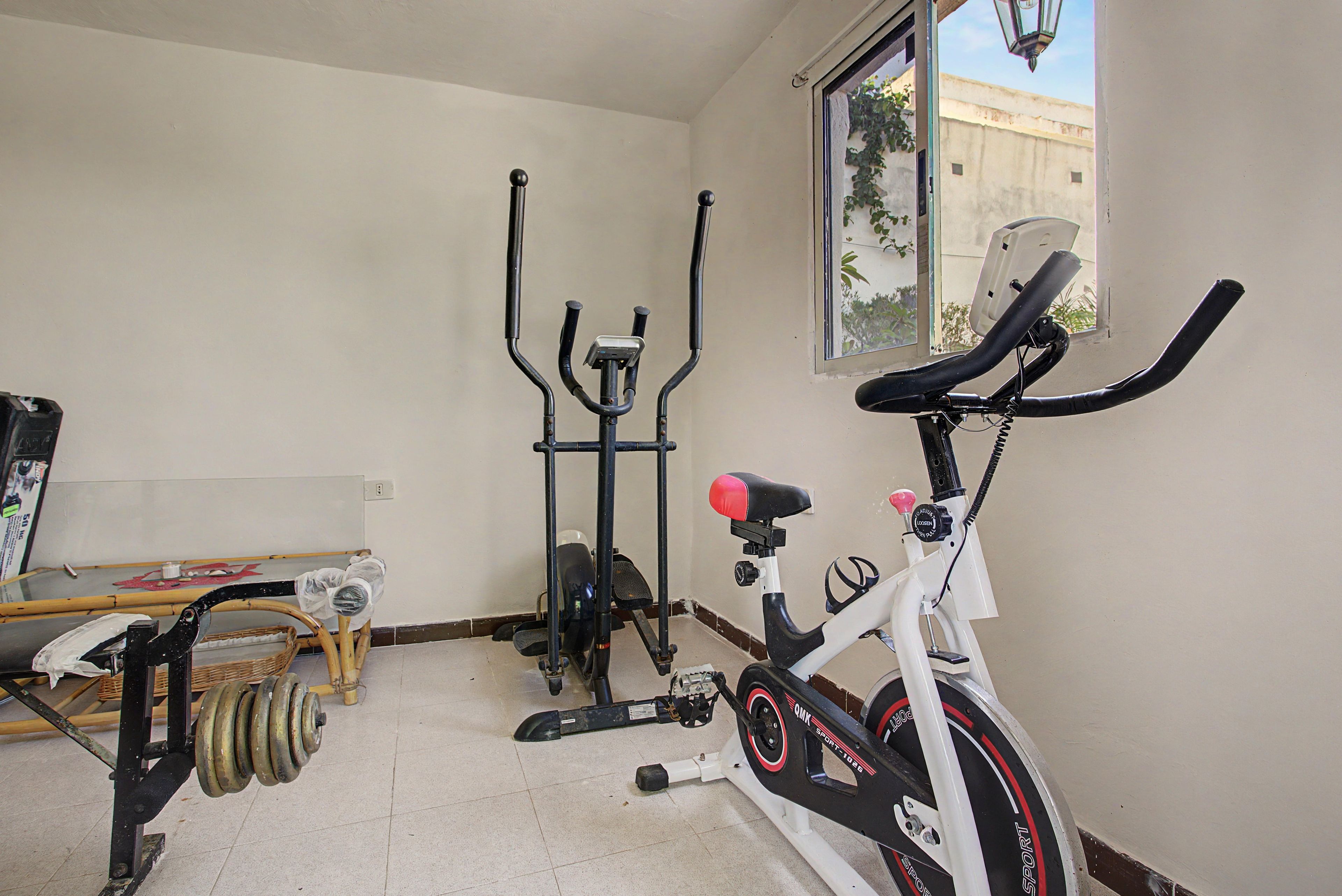 Una habitación con una bicicleta estática, una máquina elíptica y una ventana que ofrece vistas a edificios.