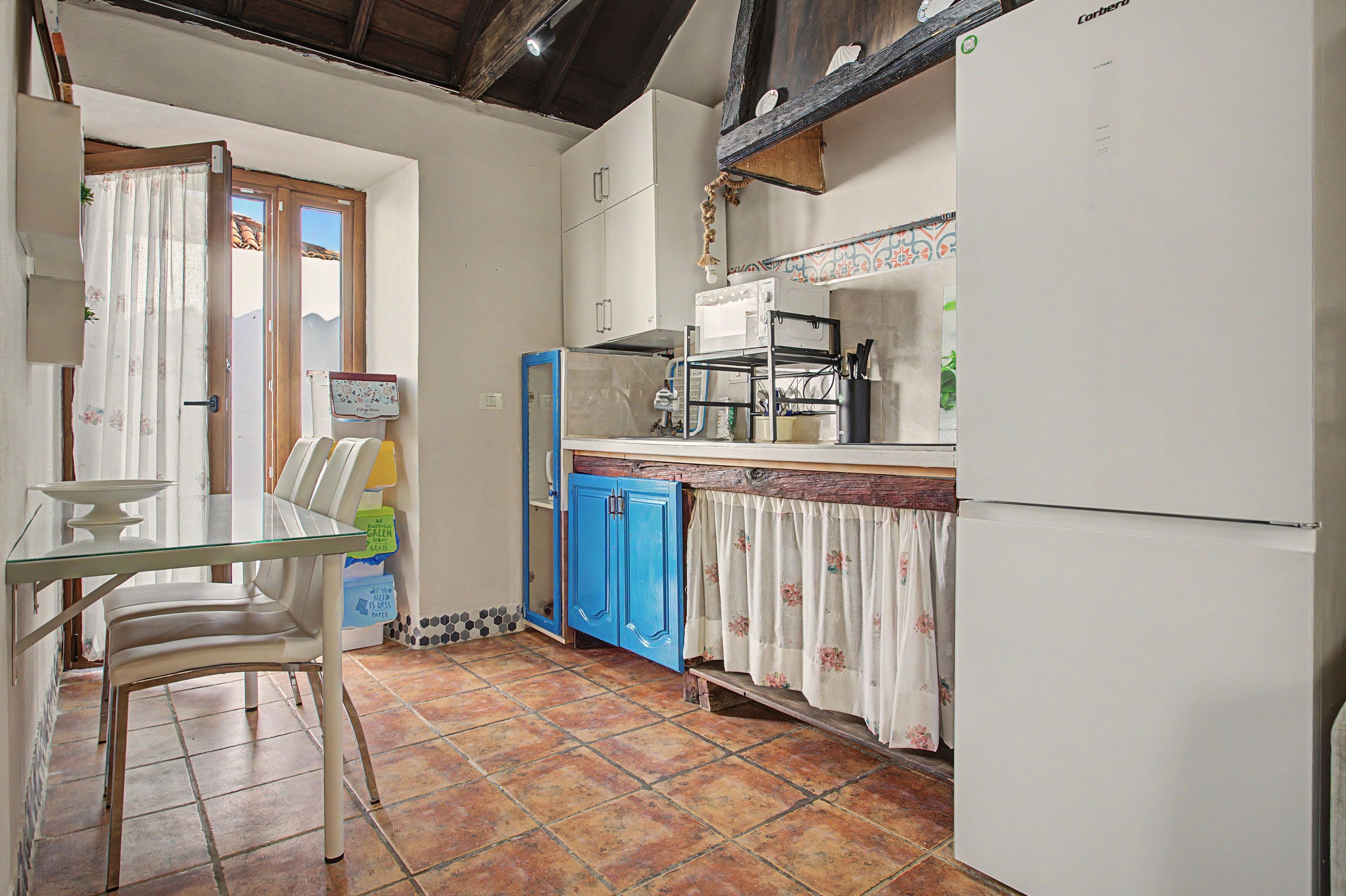 Una cocina compacta con una mesa de comedor, sillas, un armario azul y un refrigerador.