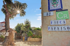 Une scène de rue avec un arbre, une clôture et un bâtiment dont le mur est recouvert de carreaux et sur lequel on peut voir des enseignes.