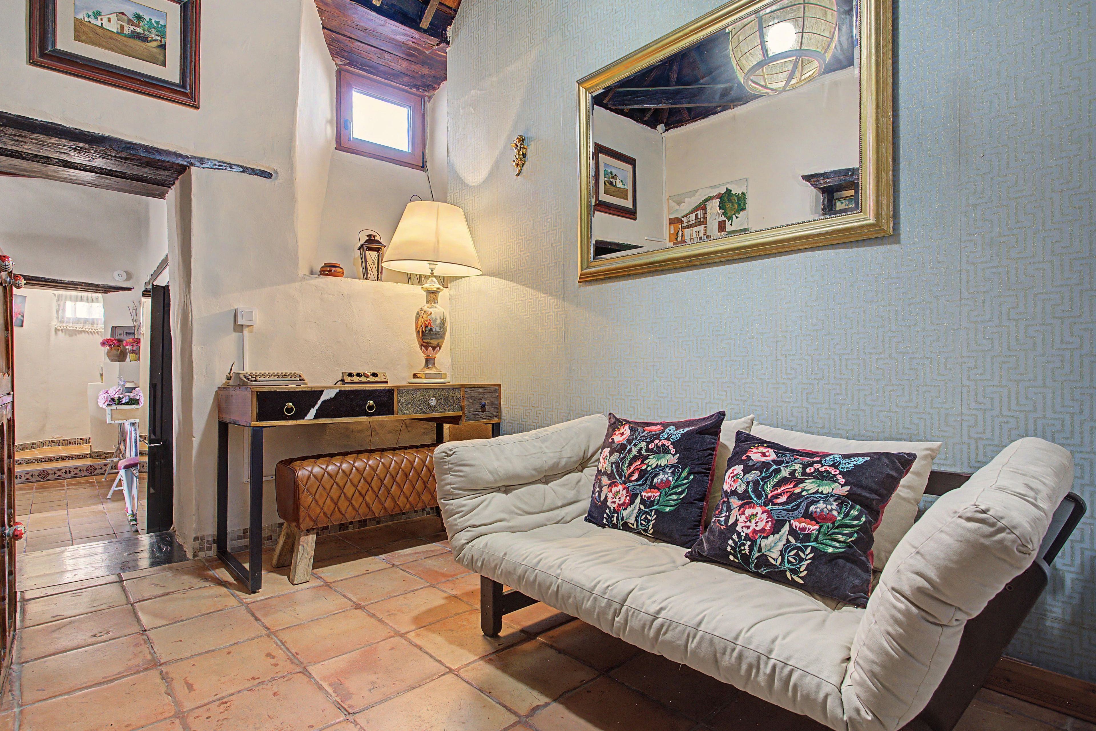 Una habitación con un sofá blanco, una mesita con una lámpara y un espejo en la pared.
